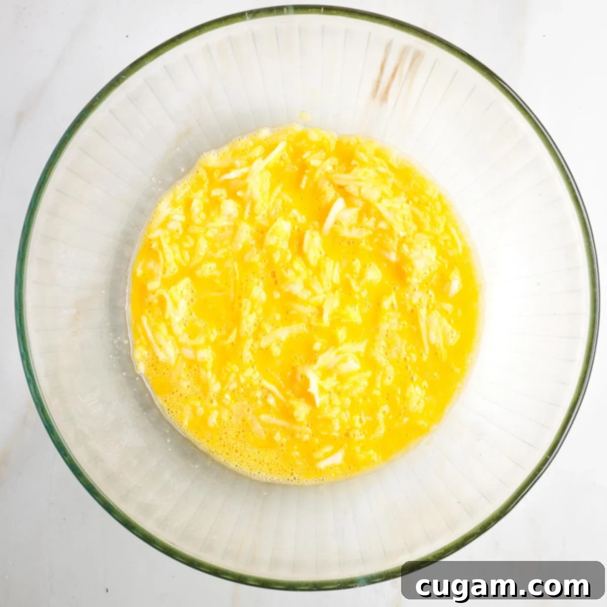 Grandma's Secret Potato Latkes 5 Whisked eggs with shredded onions in a glass bowl.