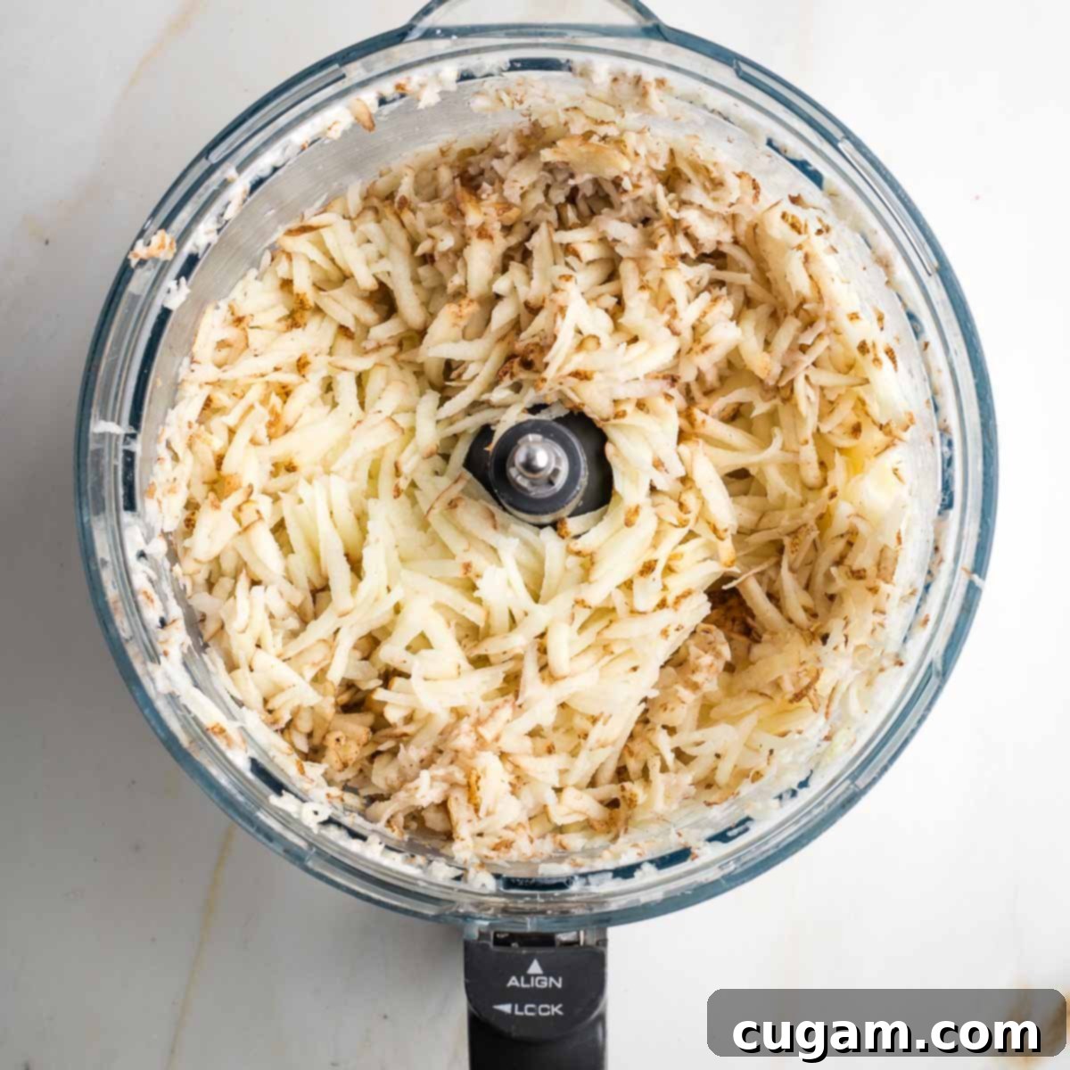 Grandma's Secret Potato Latkes 7 Shredded russet potatoes in the bowl of a food processor.