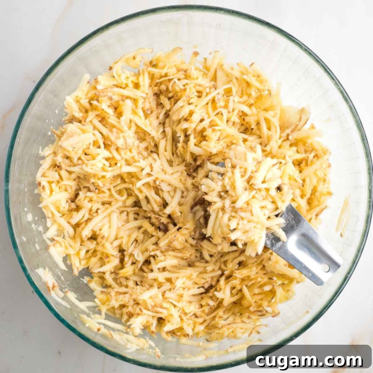 Grandma's Secret Potato Latkes 9 ¼ cup measure scooping out some potato latke mixture from a large glass bowl.