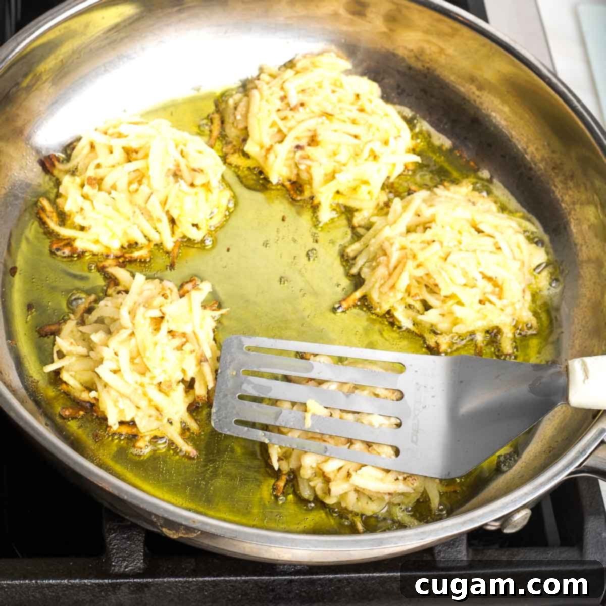 Grandma's Secret Potato Latkes 10 Spatula pushing down potato latke in a large skillet full of oil and latkes.