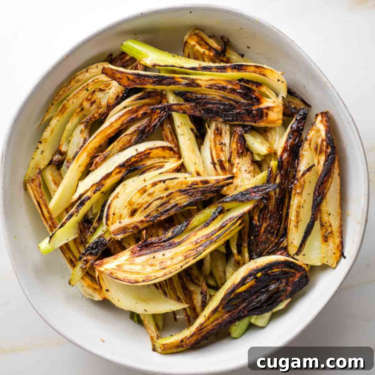 Seared golden-brown fennel wedges resting in a white bowl after being removed from the skillet.