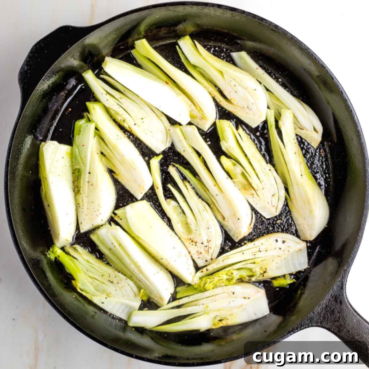 Fennel wedges generously seasoned with salt and pepper, arranged in a hot cast iron skillet.