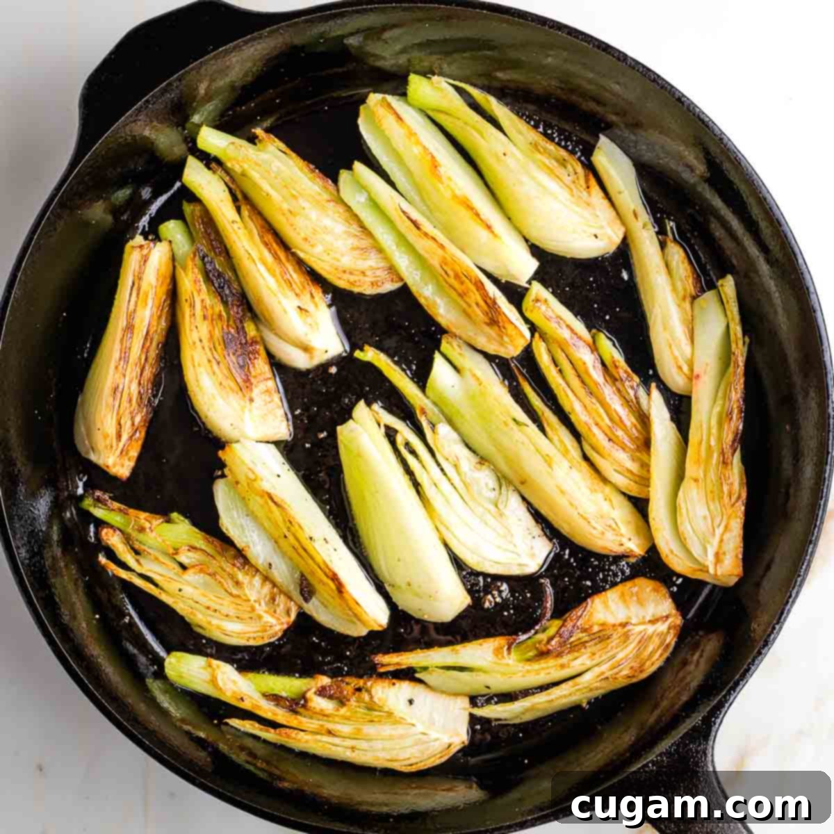 Perfectly browned fennel wedges cooking in a cast iron skillet.