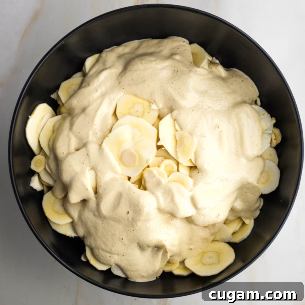 Black bowl with thin slices of parsnips, covered in cream sauce.
