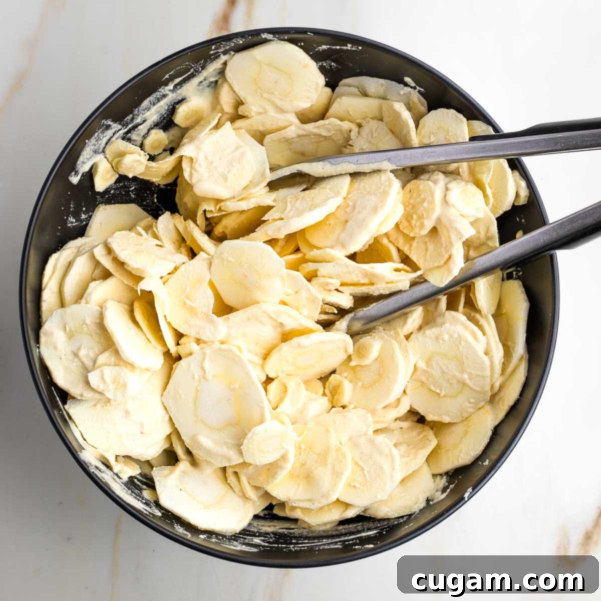 Tongs tossing sliced parsnips with cream sauce. 