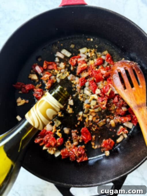 Pouring white wine into the pan with diced shallots, garlic, and sun-dried tomatoes to deglaze