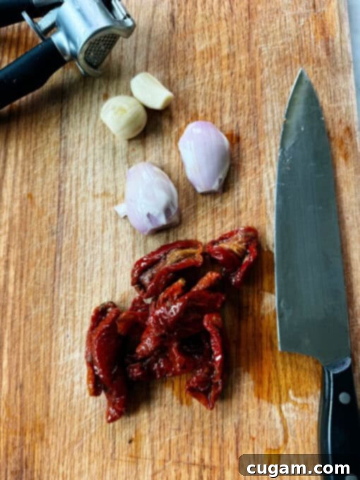 Shallot, garlic, and sun-dried tomatoes on a chopping board with a knife
