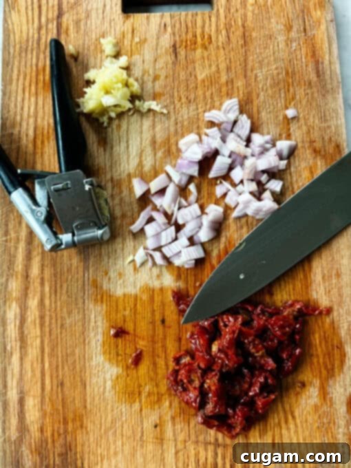 Diced shallot, minced garlic, and chopped sun-dried tomatoes on a chopping board