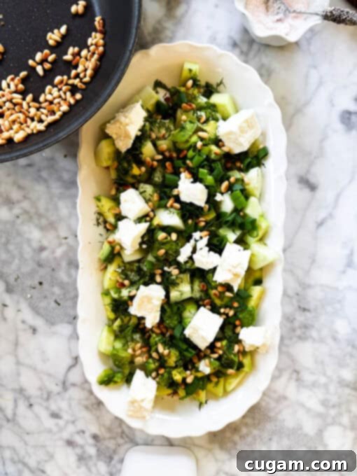 Golden toasted pine nuts are scattered over the assembled cucumber feta salad, adding a rich, nutty crunch.