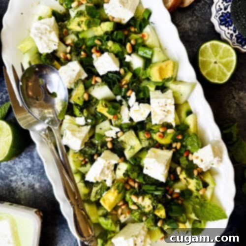 Overhead view of a platter of cucumber feta salad, vibrant green and white with hints of fresh herbs, ready to serve.