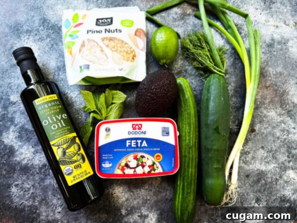Fresh ingredients laid out for cucumber and feta salad, including cucumbers, avocado, a block of feta, fresh herbs, and pine nuts.