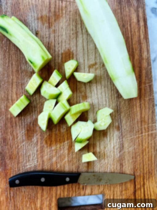 A crisp green cucumber, partially peeled and cut into perfect rounds on a wooden chopping board, ready for the salad.