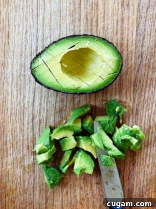 Overhead view of half a ripe Hass avocado next to a pile of neatly sliced avocado cubes, vibrant green and ready to be added to the salad.