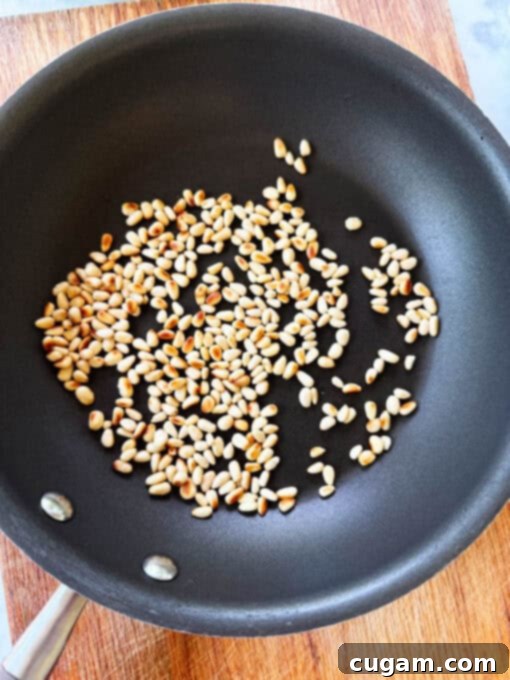 Pine nuts being gently toasted in a hot skillet on the stove, turning lightly golden for the cucumber feta cheese salad.