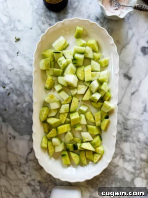 Neatly cubed cucumber pieces arranged on a crisp white serving plate, forming the base of the refreshing salad.