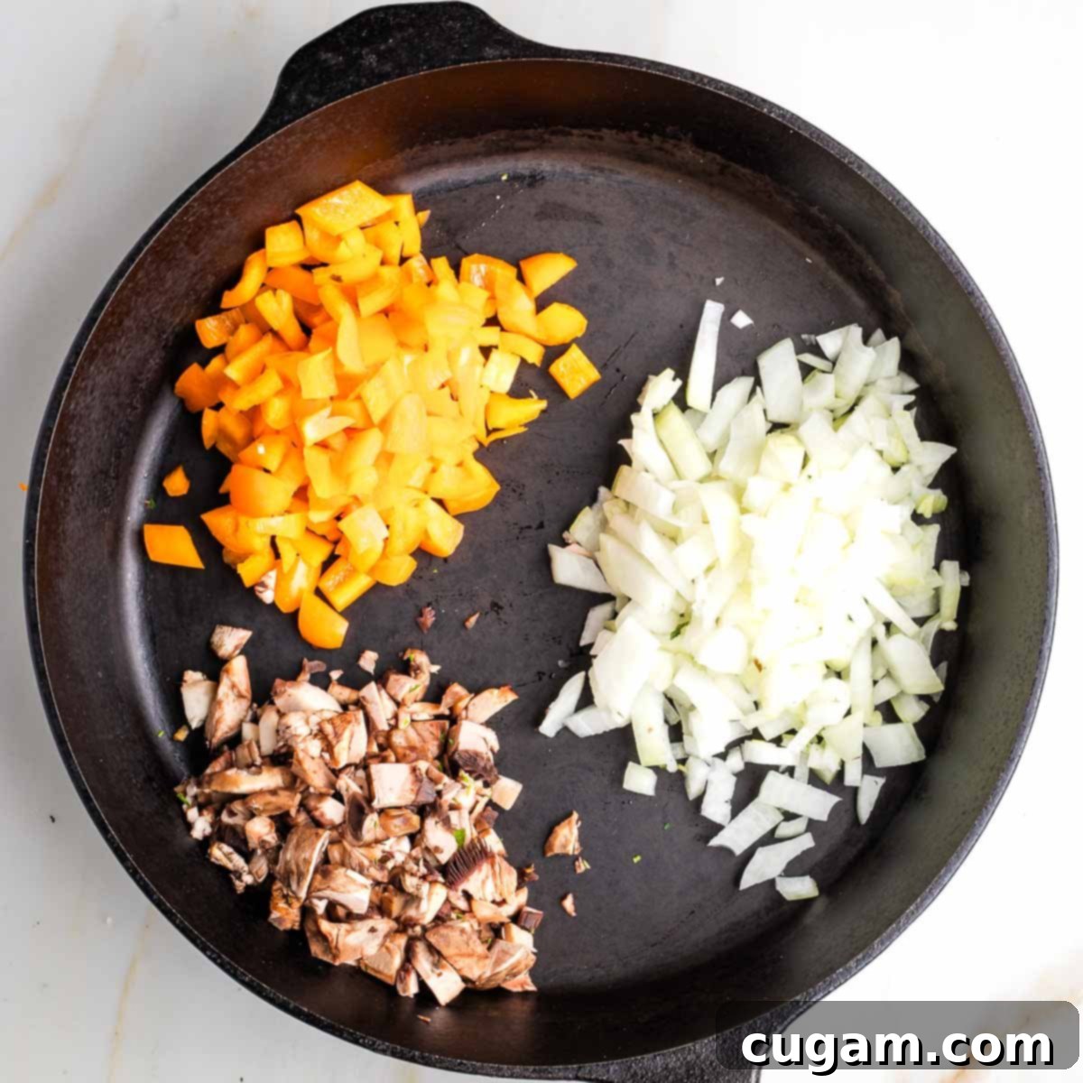 Cast iron skillet with diced orange pepper, onion, and mushroom stems.