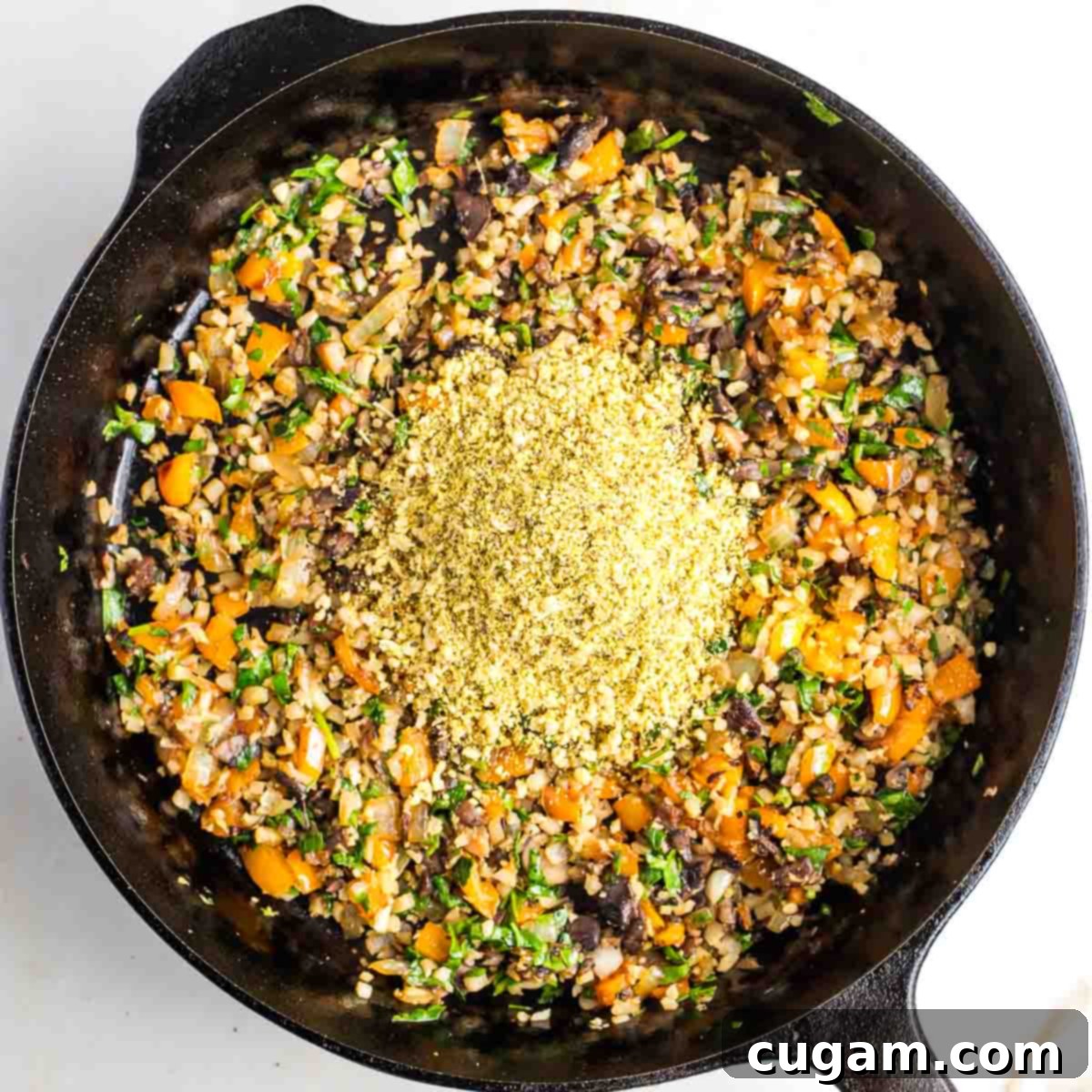 Sauteed diced vegetables and greens in a cast iron skillet with a heap of yellow powder in the center.