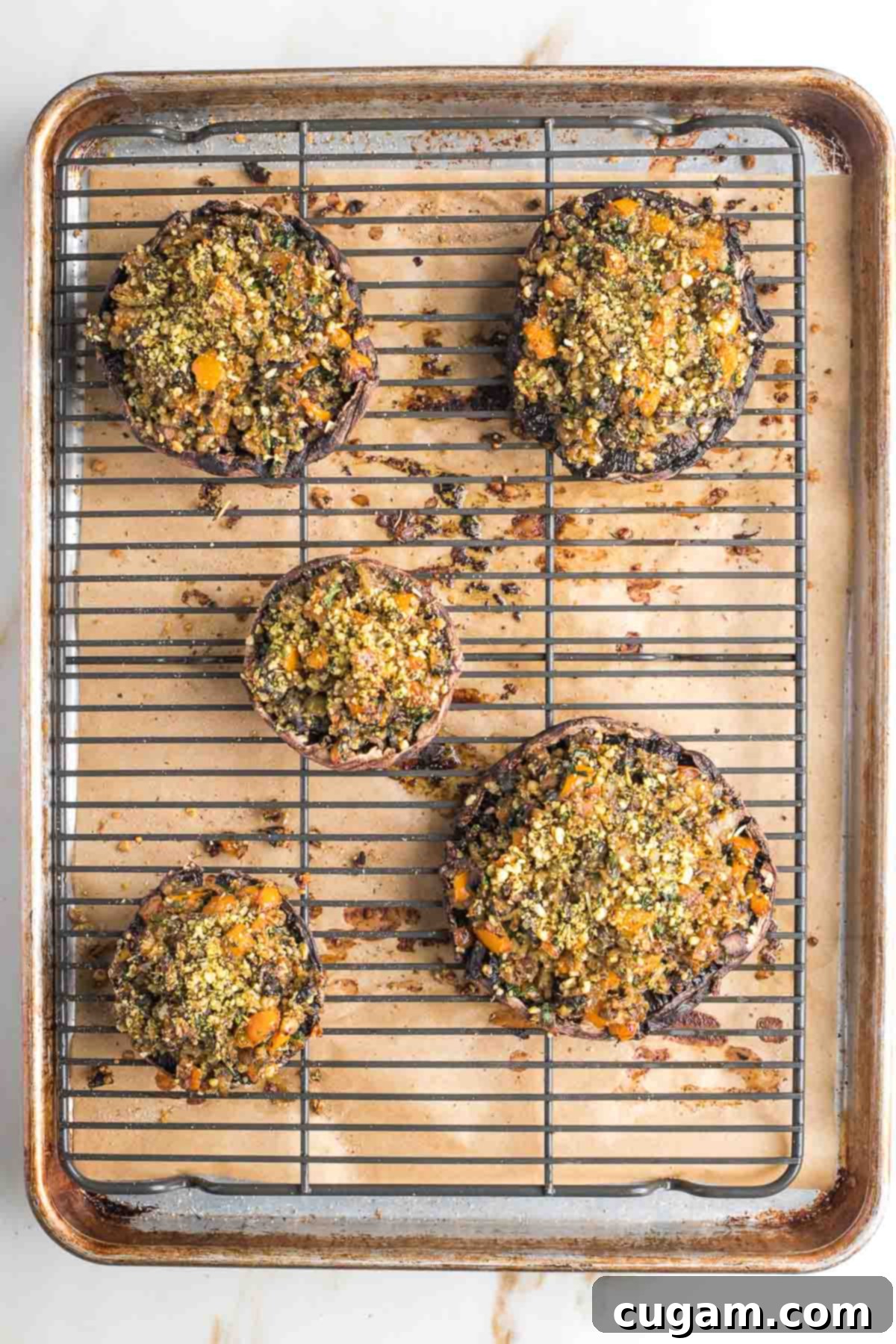 Three stuffed portobello mushrooms on a serving dish, one on an individual plate, garnished with fresh herbs.