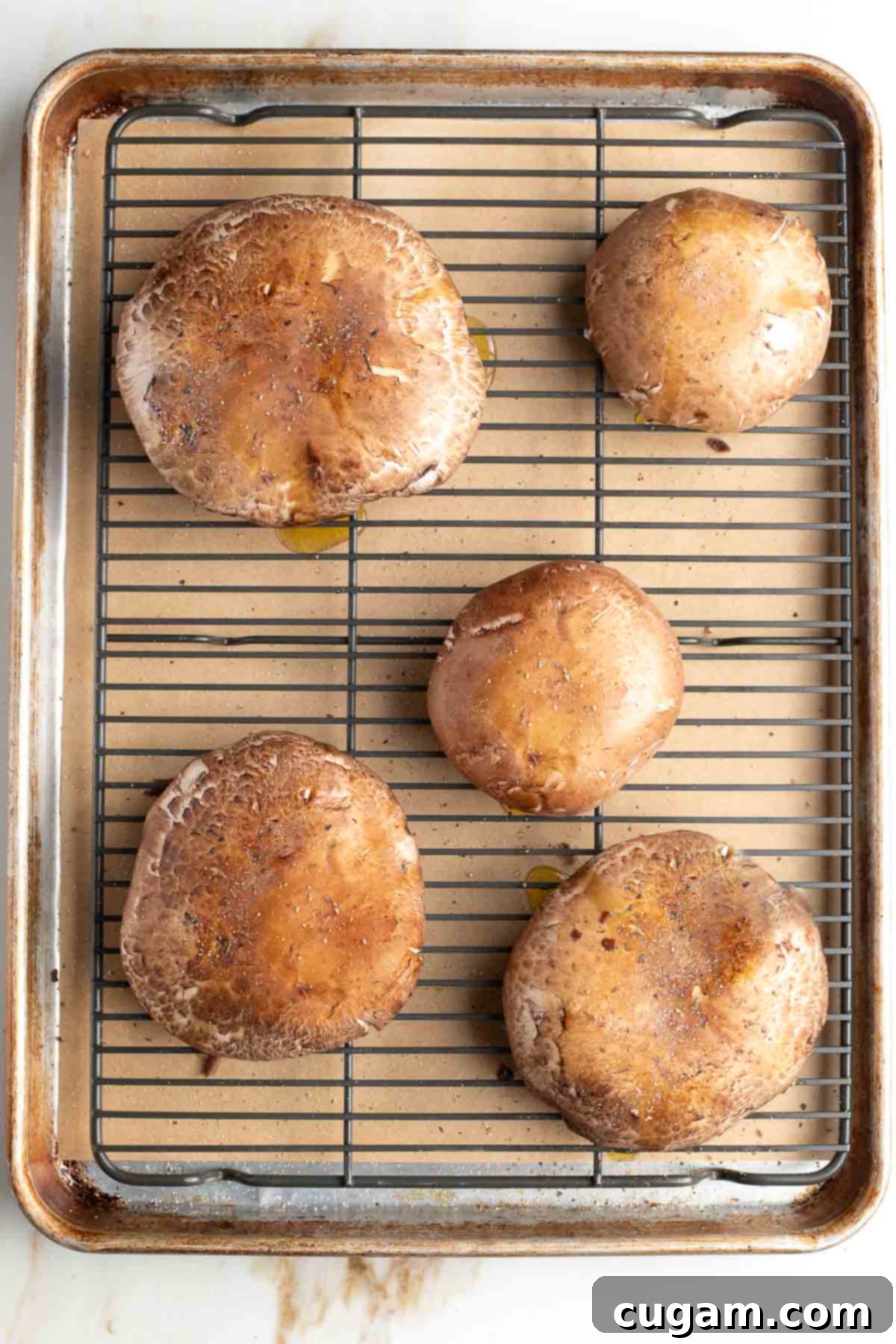 Portobello mushroom caps on a wire rack that's on a baking tray. 