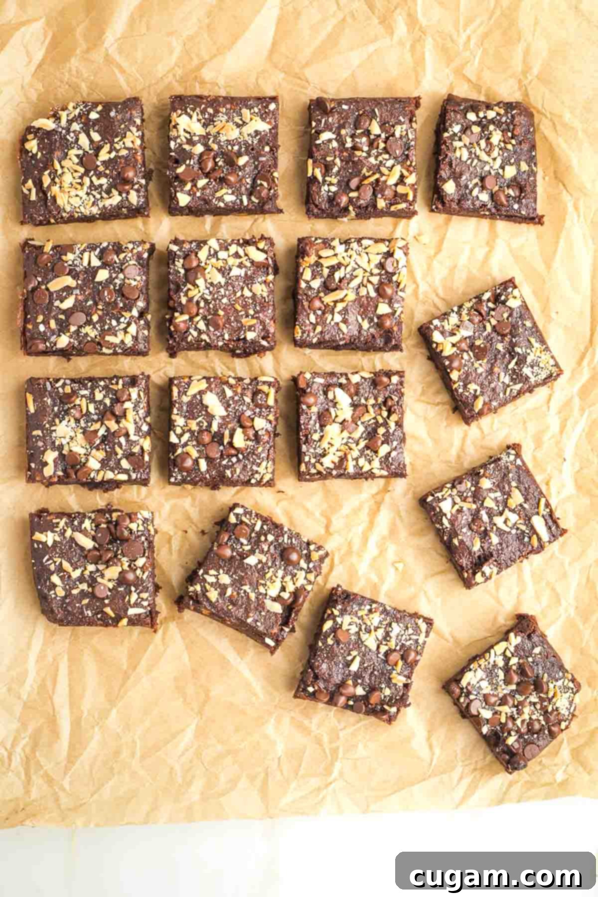 Brownie squares with nuts and chocolate chips on top in random pattern on parchment paper.