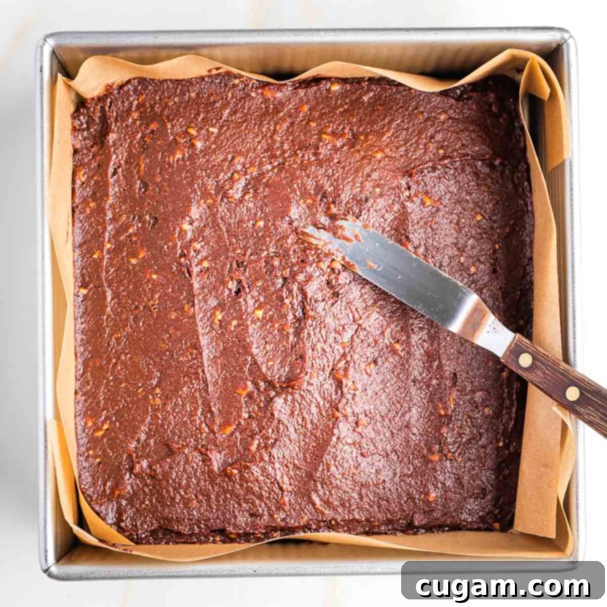 Offset spatula spreading brownie batter into a square baking pan. 