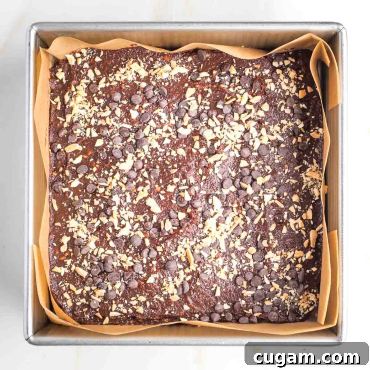 Brownie batter, sprinkled with nuts and mini chocolate chips in a square baking pan.