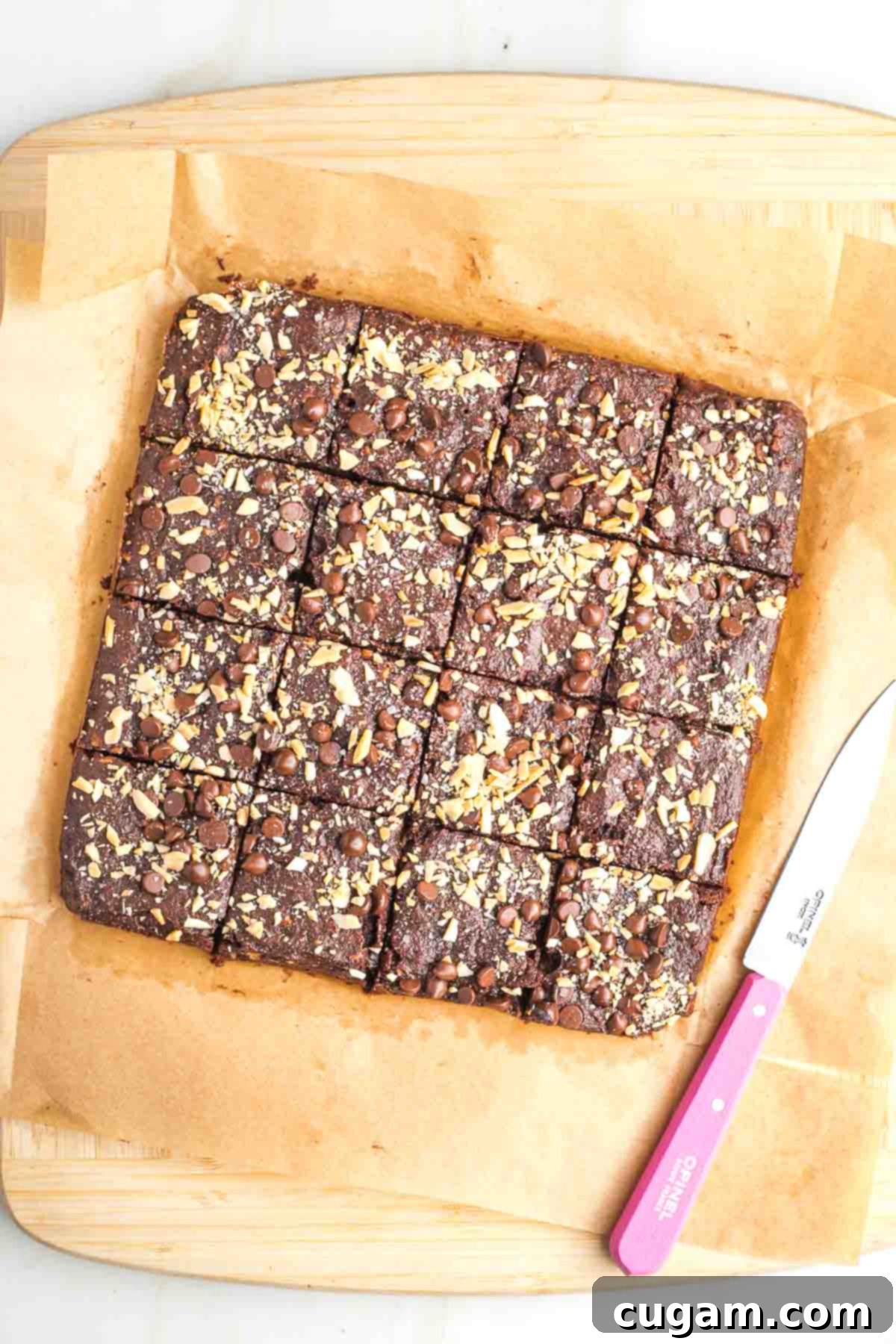 Brownies, sprinkled with nuts and chocolate chips, cut into squares with a pink knife. 