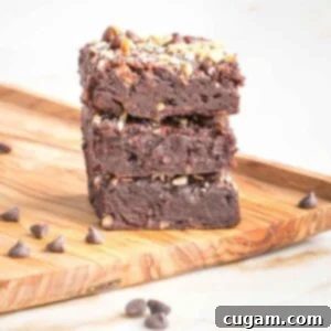 Stack of three chocolate brownies topped with chocolate chips and nuts.