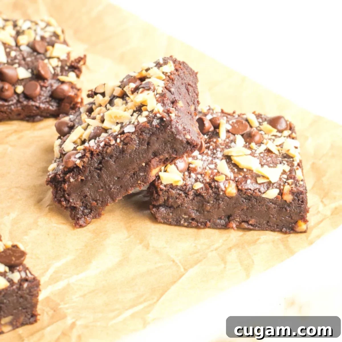Two brownies, topped with chocolate chips and crushed almonds, laying on their side so you can see the fudgey interior.