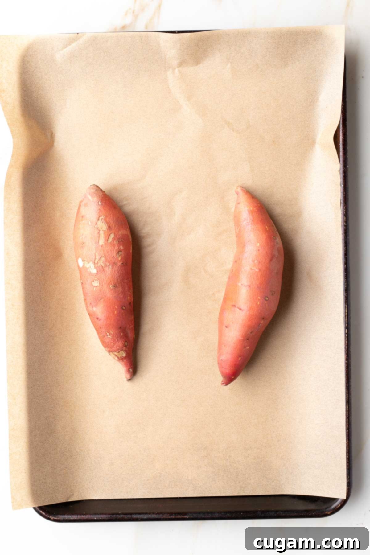 Two sweet potatoes on a baking sheet lined with parchment paper. 