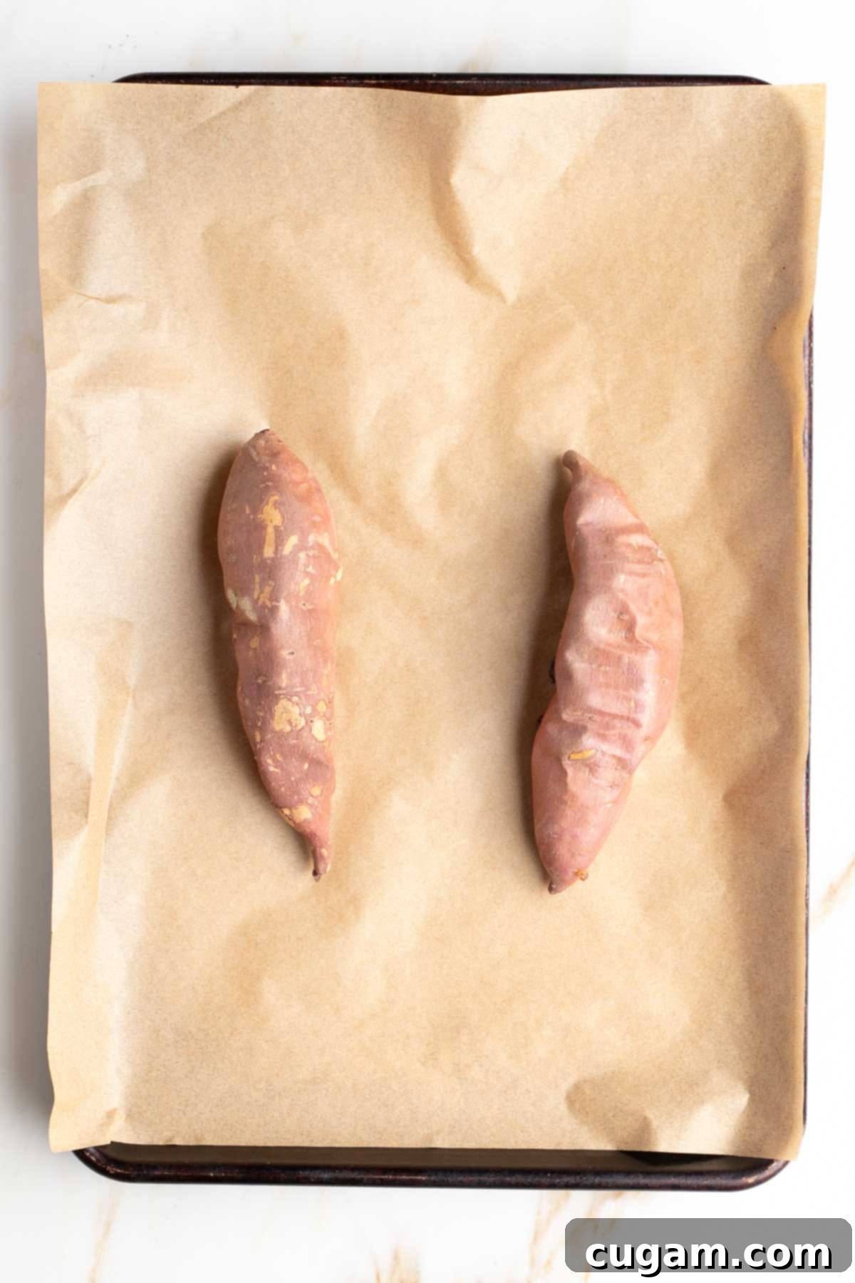 Two baked sweet potatoes on a parchment lined baking tray.
