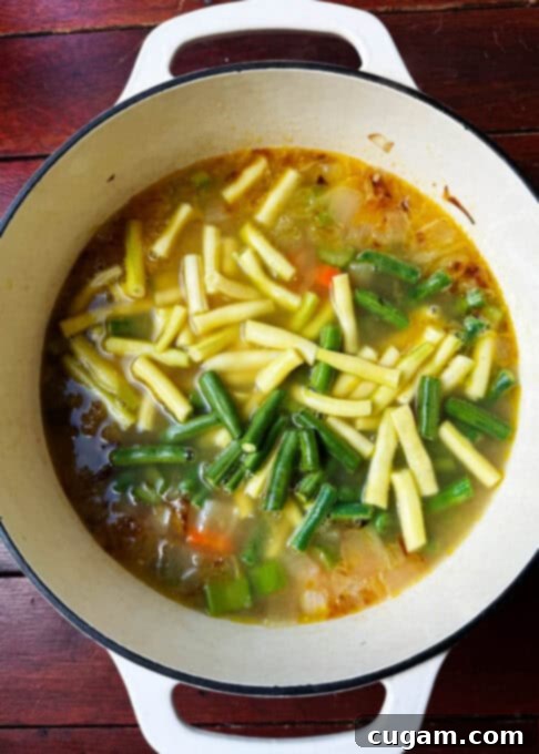 Yellow and green string beans added to the simmering soup pot with other vegetables