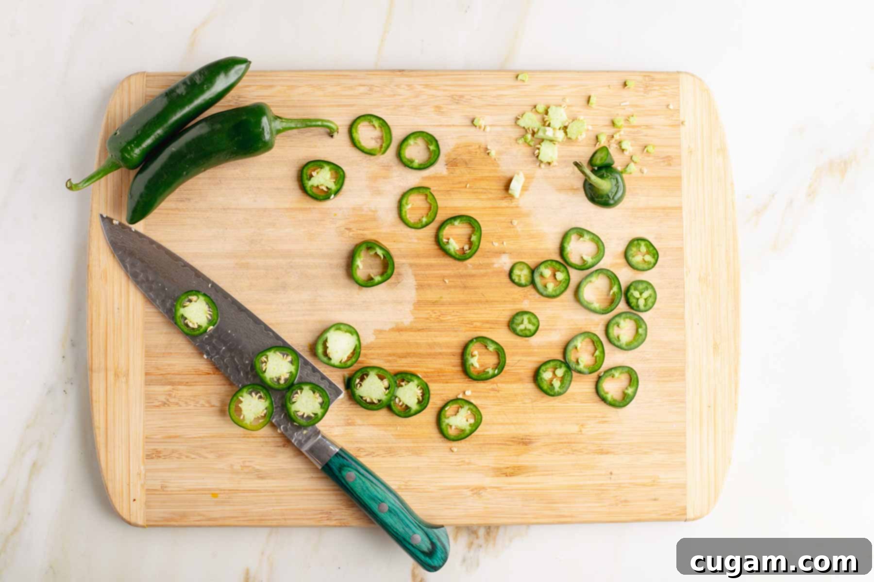 Slicing jalapenos into thin rounds and removing the seeds and membranes on a wooden board.