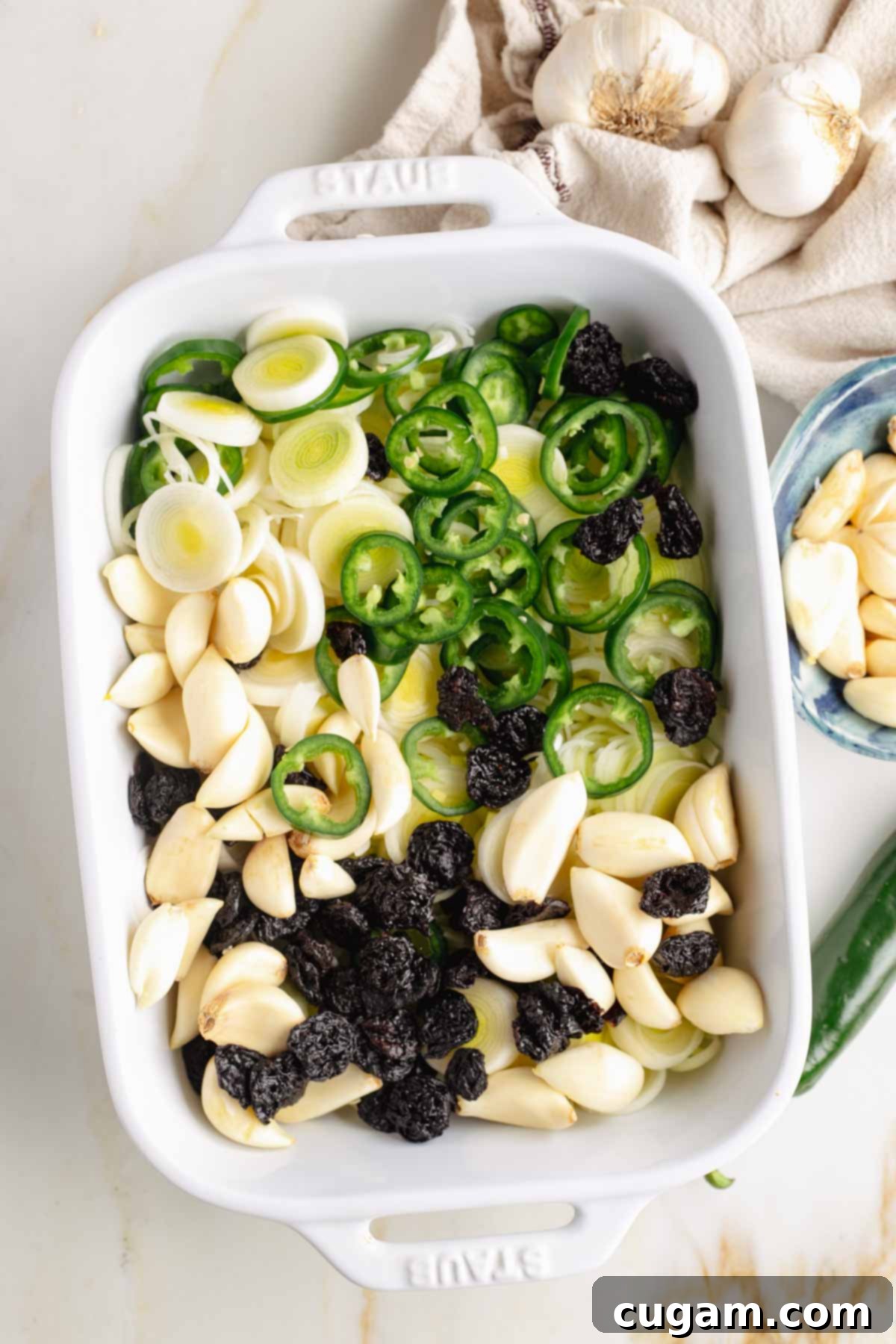 Baking dish with garlic cloves, jalapeno slices, dried cherries and sliced leeks.