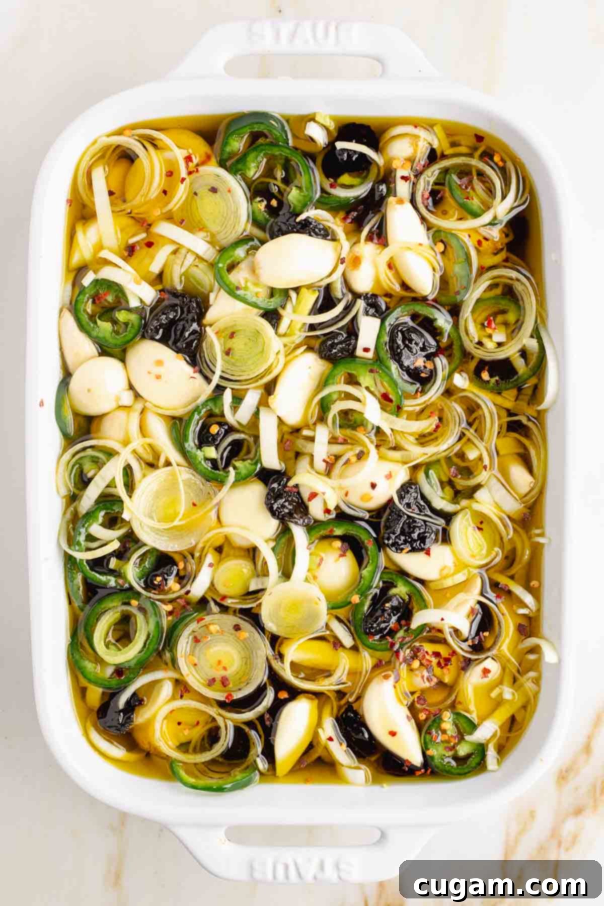 Garlic cloves, sliced leek and jalapenos plus dried cherries, covered in oil in a shallow baking dish.