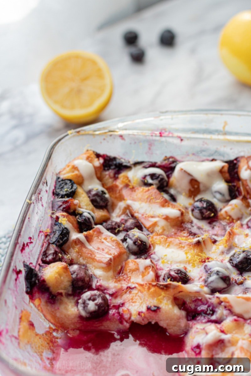 Baked lemon blueberry bread pudding in glass pan on marble with lemons and blueberries.