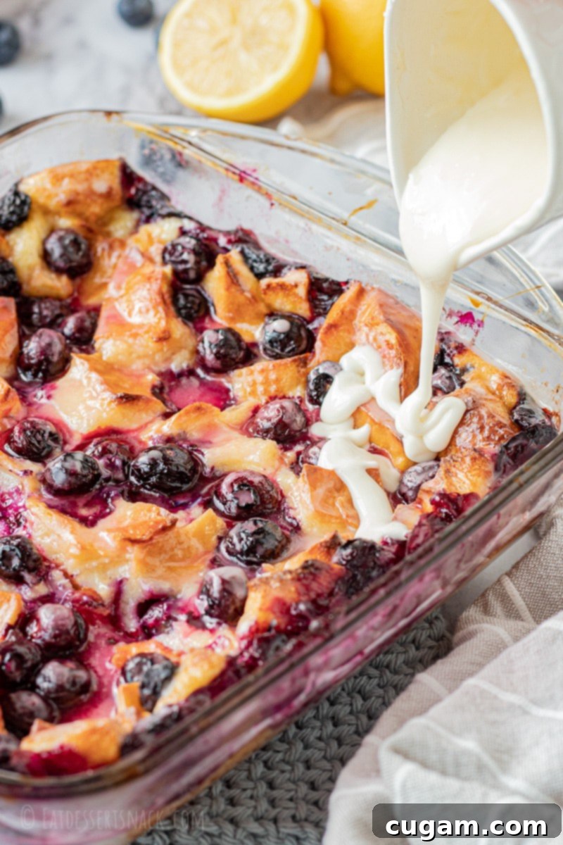 Baked lemon blueberry bread pudding in glass pan with lemon icing pouring on top.