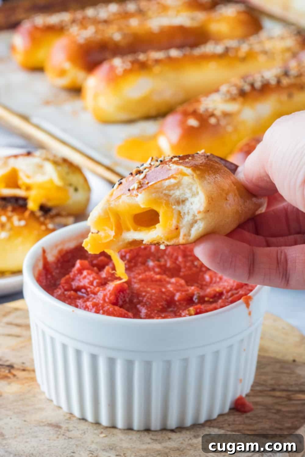 half of a baked cheese pretzel above white bowl of pizza sauce. 