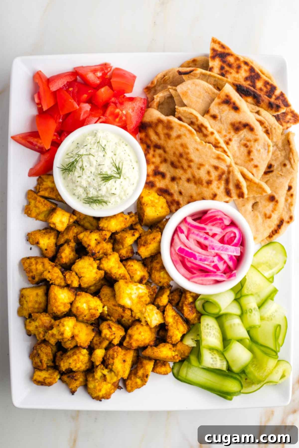 Platter with tofu shawarma, pita, cukes, tomatoes, pickled onions and tzatziki.