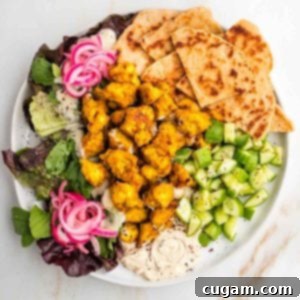 Tofu shawarma on a plate with pita, cucumbers, hummus, pickle red onions and leafy greens.