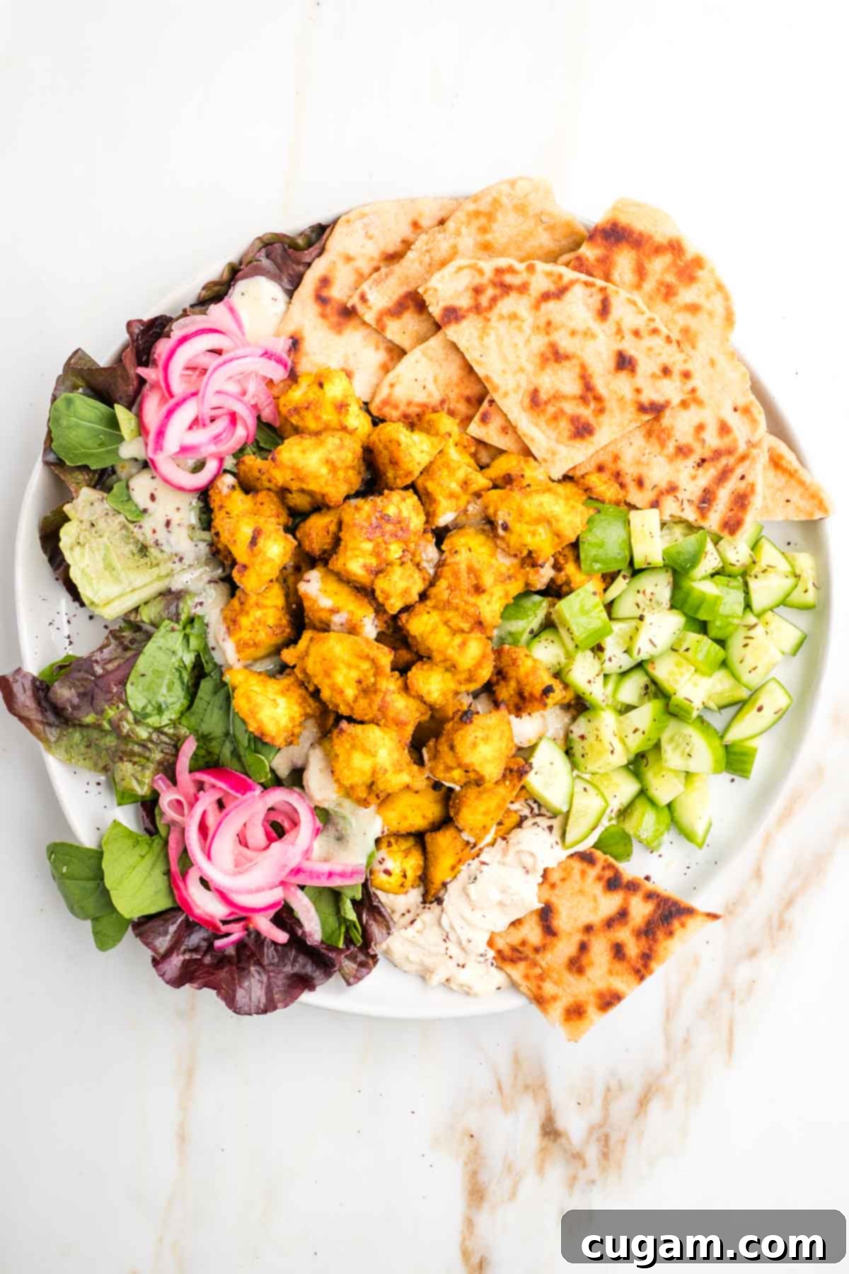 Platter of pita, tofu shawarma, lettuce, pickled onions, hummus and cucumbers.