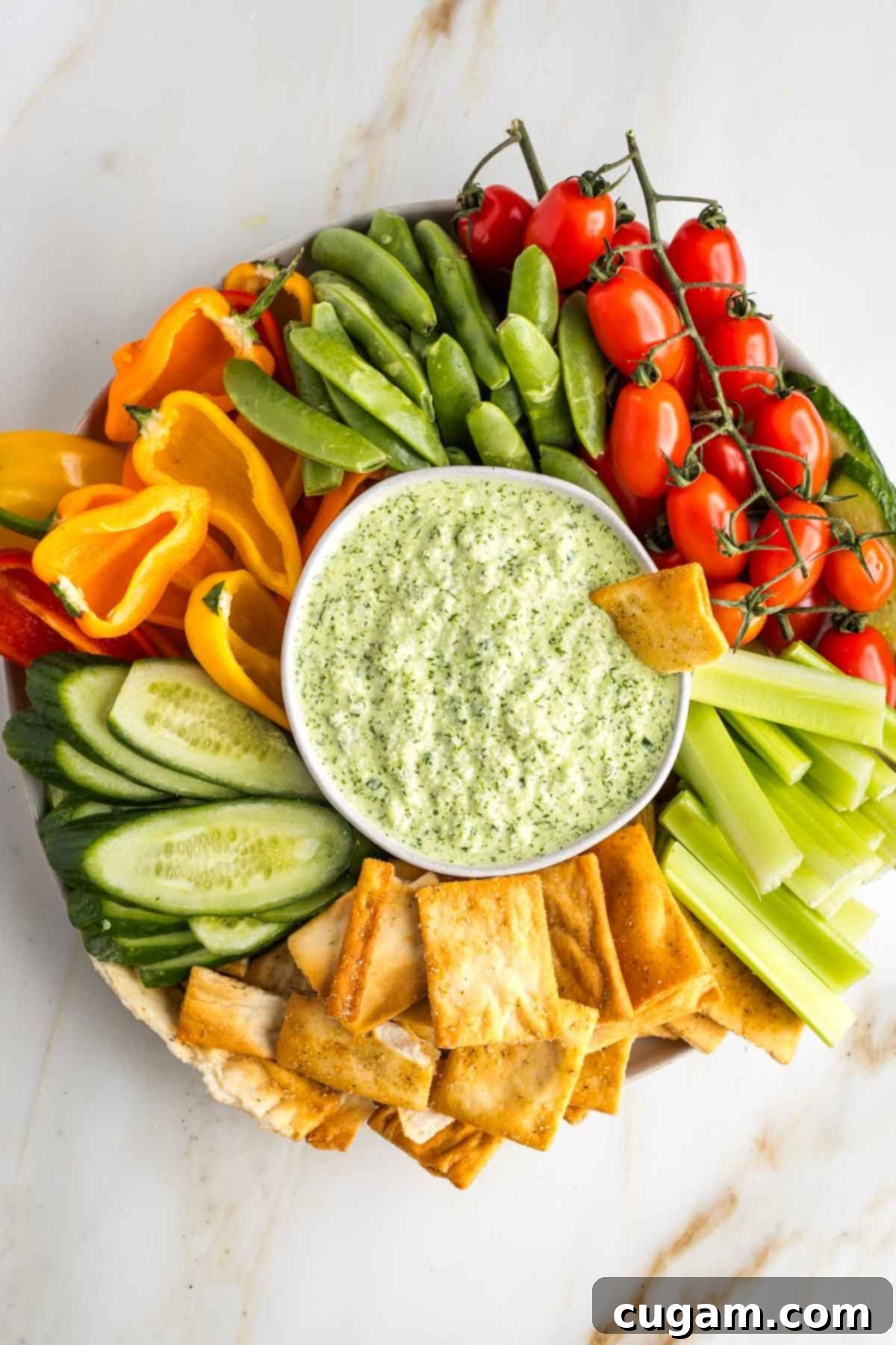 Green tzatziki dip in a bowl, surrounded by colorful veggies on a platter.