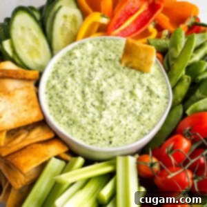 Creamy green dip in a bowl, surrounded by colorful vegetables.