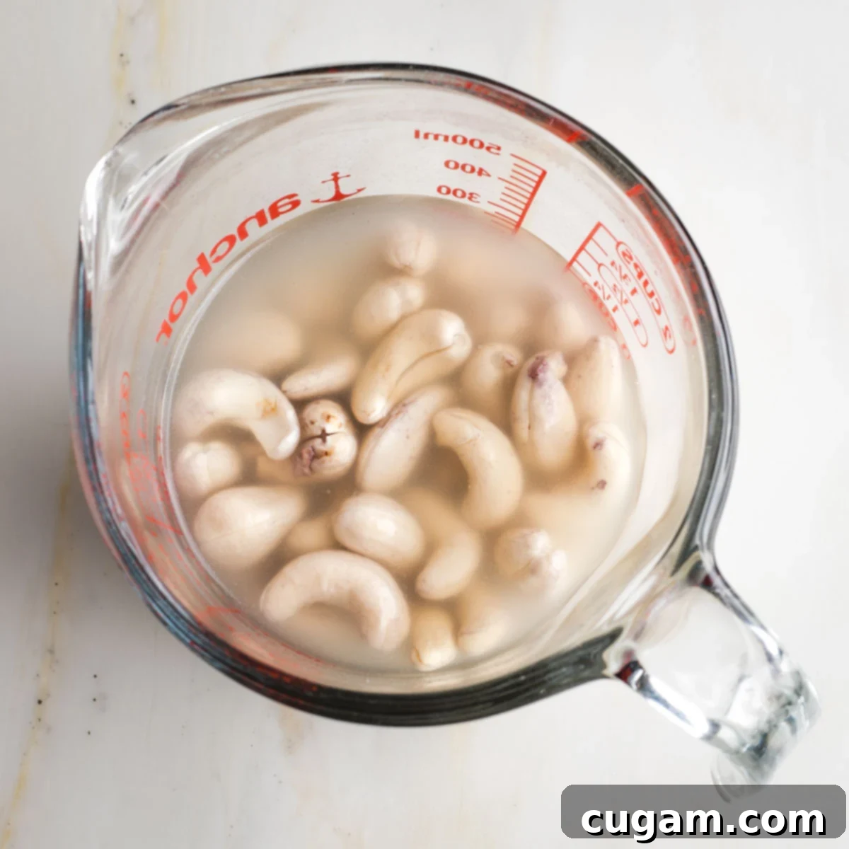 Glass measuring cup with water covering raw cashews. 