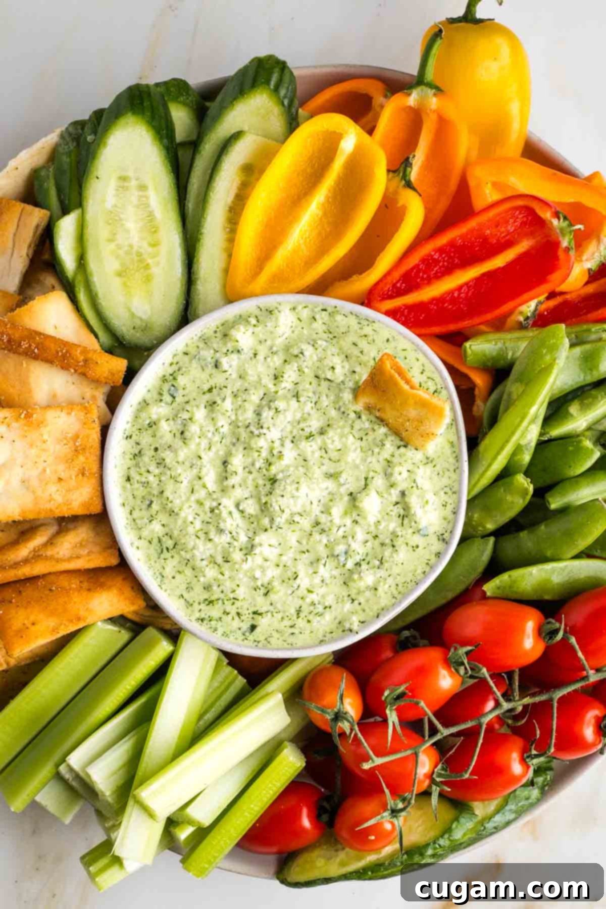 Dairy free tzatziki in a bowl surrounded by colorful vegetables and pita chips. 