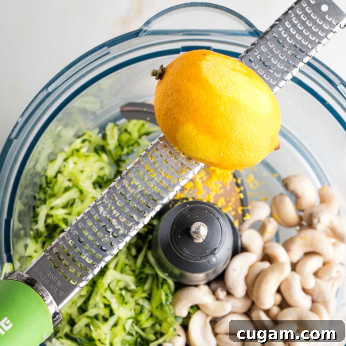 Zesting a lemon over a food processor filled with cashews and grated cucumber.