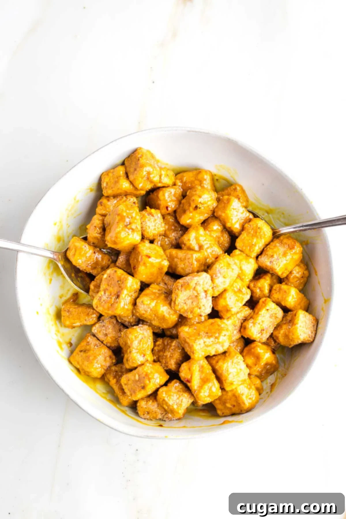 Cubes of crispy tofu in a bowl, smothered in orange sauce.