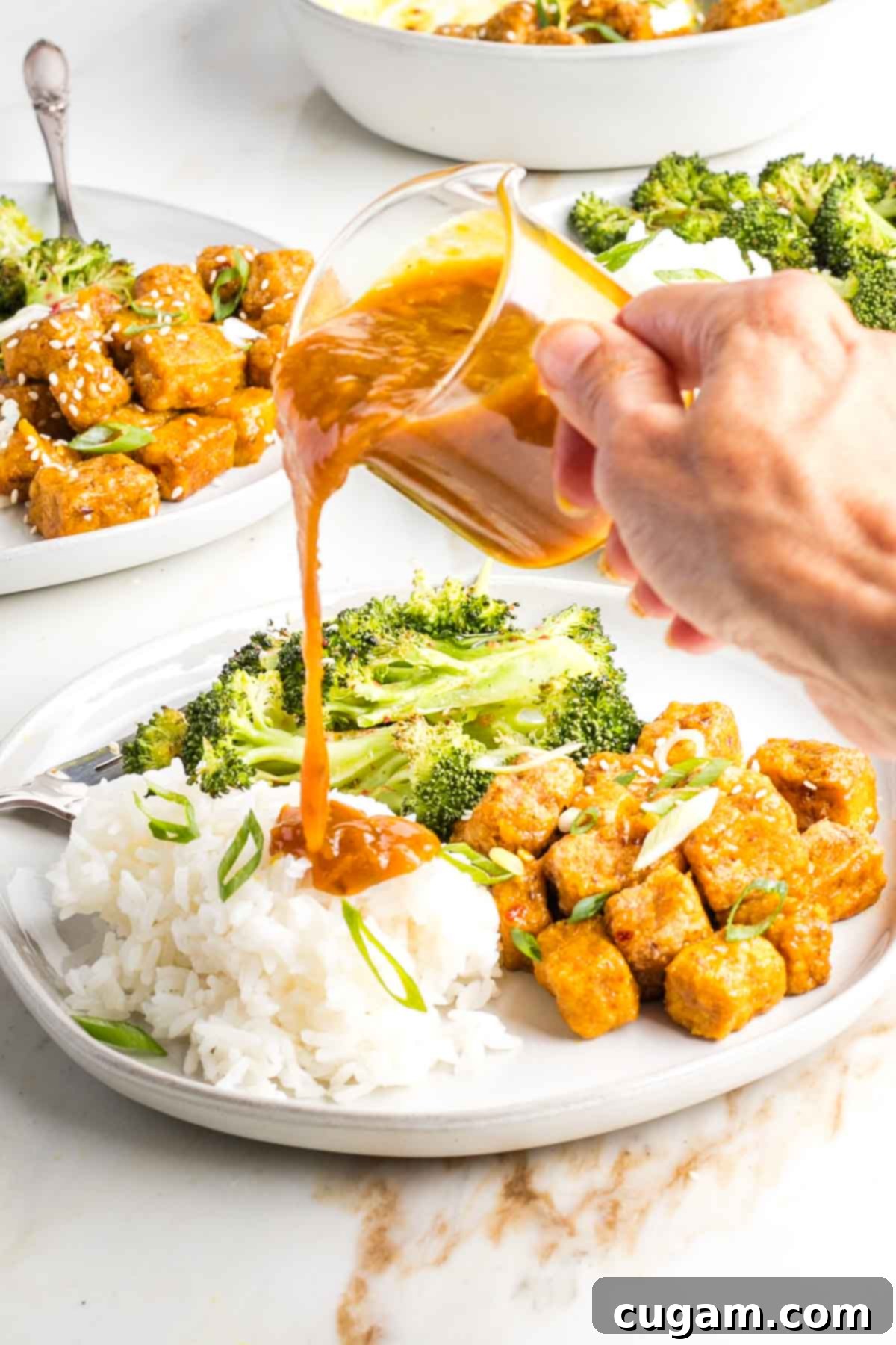 Extra orange sauce poured onto white rice on the dish with tofu and broccoli.
