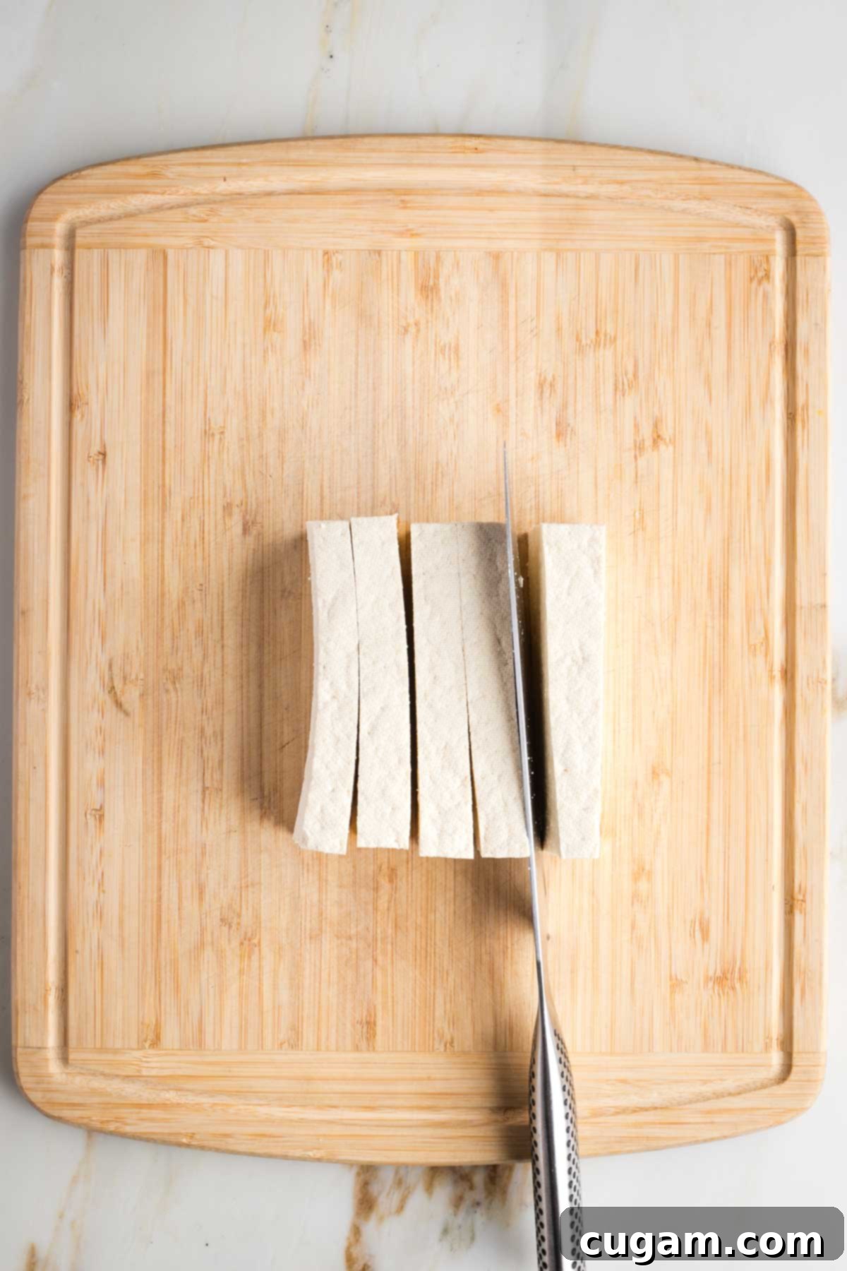 Cutting strips of tofu from a block on a cutting board.