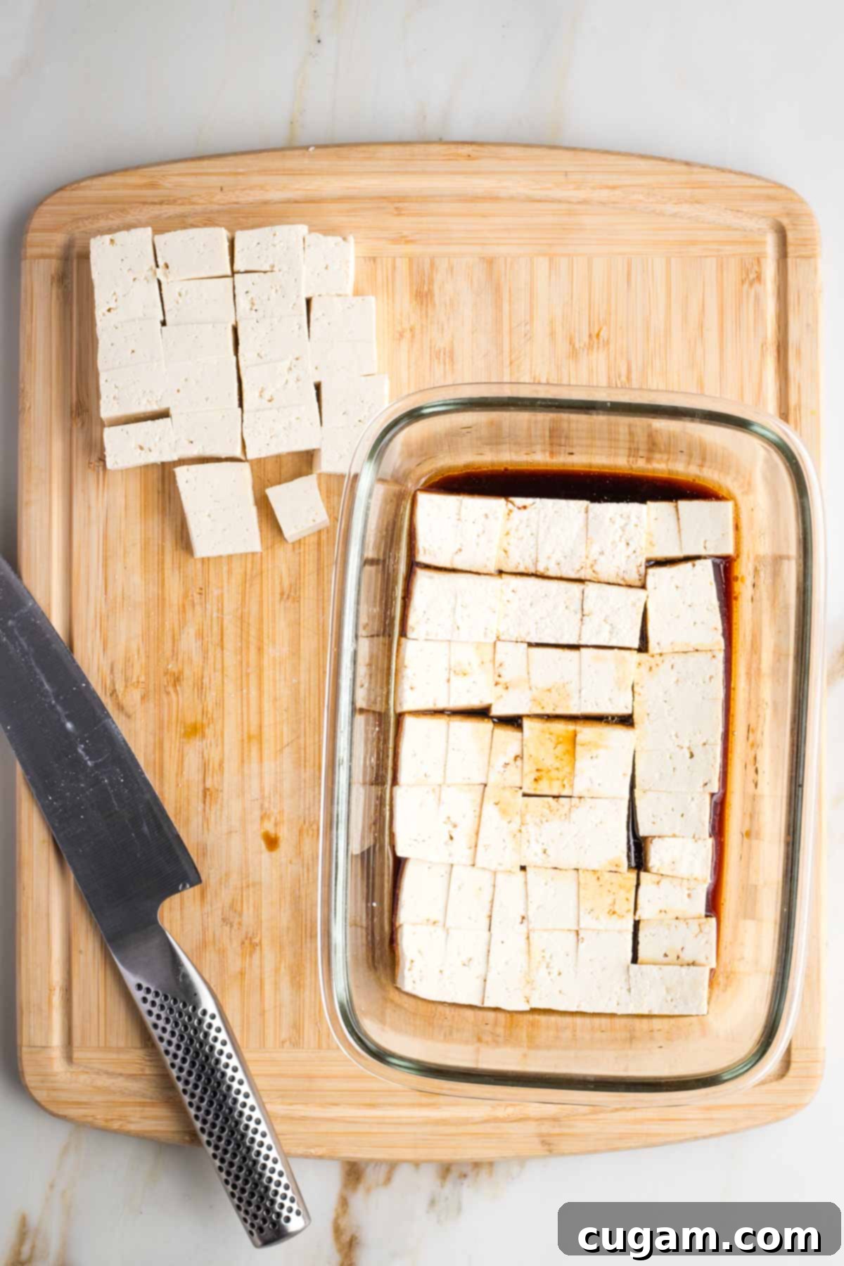 Cubes of tofu cut and then placed into a glass dish with soy sauce marinade.